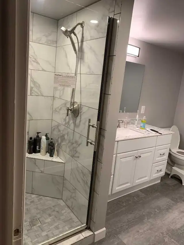 Bathroom with a marble-look tile shower behind glass, a white vanity cabinet and a toilet