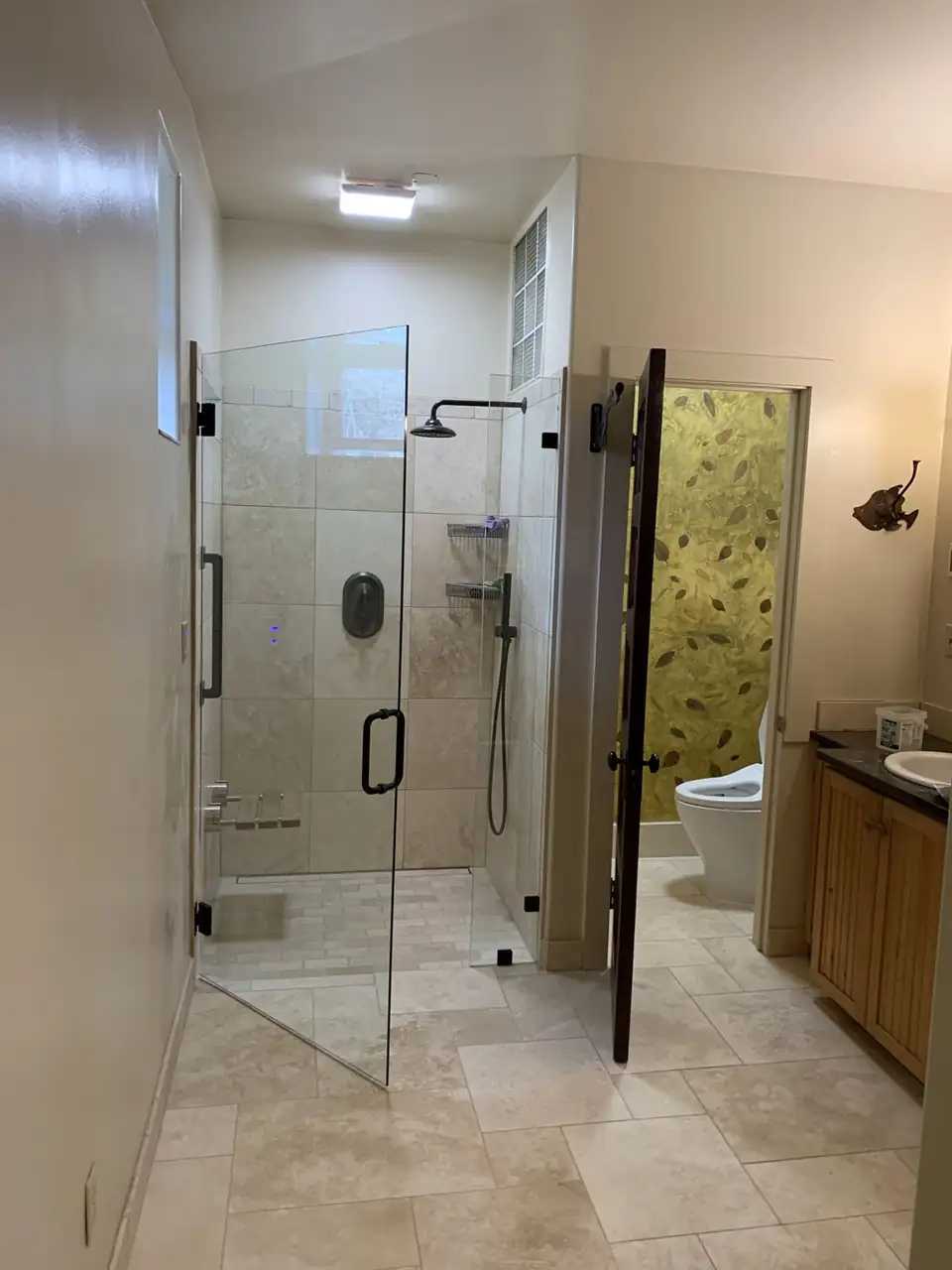 Frameless glass walk-in shower with beige tile and black fixtures, a bathroom remodel by Turnmire Eco Construction of Kettle Falls